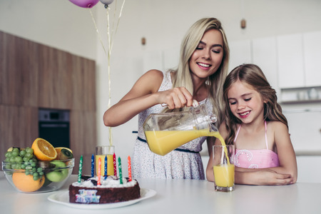 Happy family is celebrating little daughter's Birthday. Attractive young woman with her charming daughter in pink dress on kitchen.の写真素材