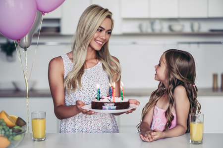 Happy family is celebrating little daughter's Birthday. Attractive young woman with her charming daughter in pink dress on kitchen.の写真素材
