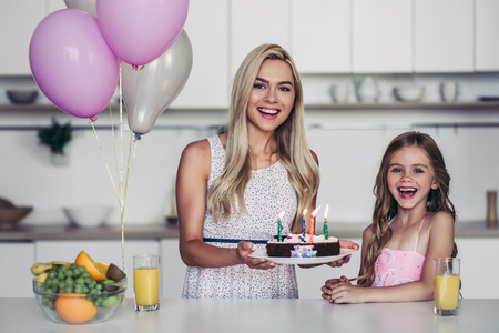 Happy family is celebrating little daughter's Birthday. Attractive young woman with her charming daughter in pink dress on kitchen.の写真素材