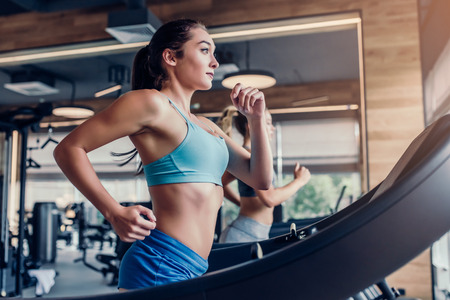 Side view of two attractive sports women on running track. Girls on treadmill