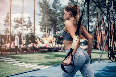 Attractive young sports woman is doing TRX training outdoors.の写真素材