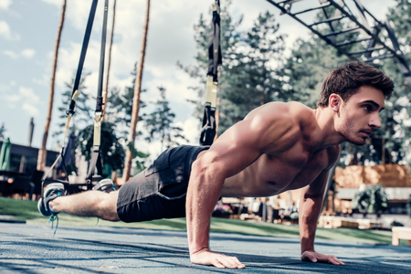 Handsome muscular man is training outdoor on TRX. Total Body Resistance Exercises. Working out at gym.の写真素材