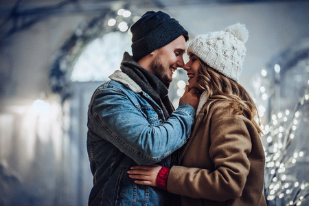 Young romantic couple is having fun outdoors in winter before Christmas. Enjoying spending time together in New Year Eve. Two lovers are hugging and kissing in Saint Valentine's Day.の写真素材