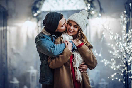 Young romantic couple is having fun outdoors in winter before Christmas. Enjoying spending time together in New Year Eve. Two lovers are hugging and kissing in Saint Valentine's Day.の写真素材