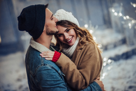 Young romantic couple is having fun outdoors in winter before Christmas. Enjoying spending time together in New Year Eve. Two lovers are hugging and kissing in Saint Valentine's Day.の写真素材