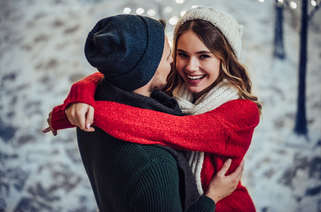 Young romantic couple is having fun outdoors in winter before Christmas. Enjoying spending time together in New Year Eve. Two lovers are hugging and kissing in Saint Valentine's Day.