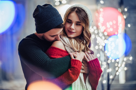 Young romantic couple is having fun outdoors in winter before Christmas. Enjoying spending time together in New Year Eve. Two lovers are hugging and kissing in Saint Valentine's Day.の写真素材