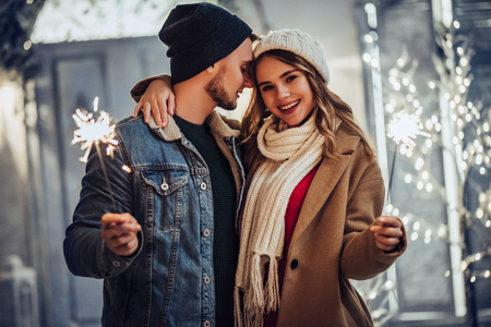 Young romantic couple is having fun outdoors in winter before Christmas with Bengal lights. Enjoying spending time together in New Year Eve. Two lovers are hugging and kissing in Saint Valentine's Dayの写真素材