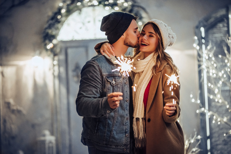 Young romantic couple is having fun outdoors in winter before Christmas with Bengal lights. Enjoying spending time together in New Year Eve. Two lovers are hugging and kissing in Saint Valentine's Dayの写真素材