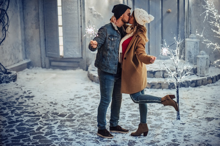 Young romantic couple is having fun outdoors in winter before Christmas with Bengal lights. Enjoying spending time together in New Year Eve. Two lovers are hugging and kissing in Saint Valentine's Dayの写真素材