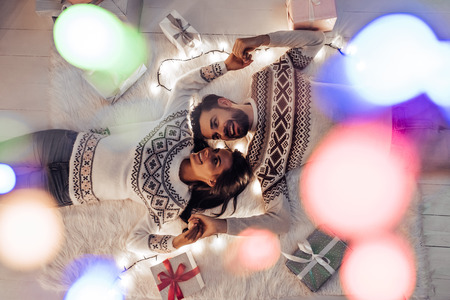 Merry Christmas and Happy New Year! Top view of beautiful couple is waiting for the New Year together while lying near beautiful Christmas tree at home.の写真素材