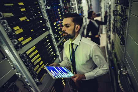 Handsome man and attractive woman are working in data centre with tablet. IT engineer specialists in...