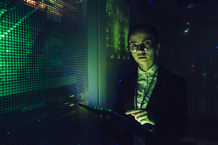 Attractive woman is working in data centre with tablet.IT engineer specialist in network server room.Running diagnostics and maintenance.Technician examining server in data center full of rack serversの写真素材