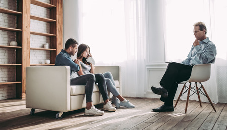 Young couple at a psychologist's reception. Solving family problems. Senior experianced psychotherapistの写真素材