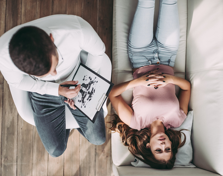 Top view of young woman is sitting on sofa during the psychotherapy session. Girl at a psychologist's reception. Experianced doctor is sitting nearby.の写真素材