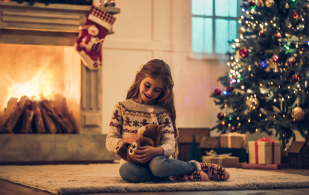 Little cute girl is waiting for Christmas at home. Charming kid with teddy bear in hands in New Year Eve.の写真素材