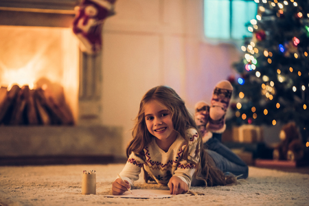 Little cute girl is waiting for Christmas at home. Charming kid is writing letter to Santa Claus in New Year Eve.の写真素材