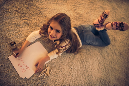 Little cute girl is waiting for Christmas at home. Top view of charming kid is writing letter to Santa Claus in New Year Eve.