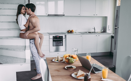 Good morning! Young romantic couple on light modern kitchen. Sexy young woman and handsome man are spending time together. Passionate lovers having sex on kitchen.の写真素材