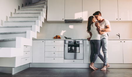 Full-length image of romantic couple at home. Attractive young woman and handsome man are enjoying spending time together while standing on light modern kitchen.の写真素材