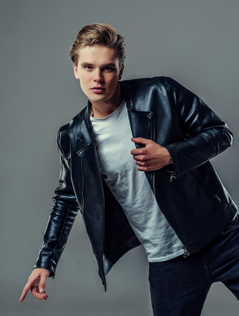 Handsome young man isolated. Fashionable  man in leather jacket is standing on grey background and looking at camera.の写真素材