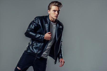 Handsome young man isolated. Fashionable  man in leather jacket is standing on grey background.の写真素材