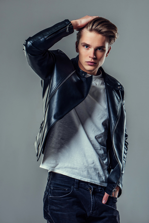 Handsome young man isolated. Fashionable  man in leather jacket is standing on grey background and looking at camera.の写真素材