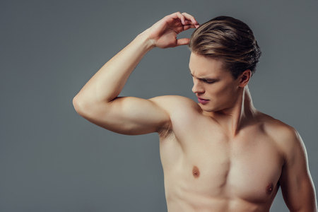 Handsome young man isolated. Portrait of shirtless muscular man is standing on grey background. Feel the smell of sweat. Men care concept.の写真素材
