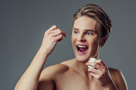 Handsome young man isolated. Portrait of shirtless muscular man is standing on grey background with 
dental floss in hands. Men care concept.の写真素材