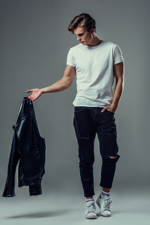 Handsome young man isolated. Fashionable  man with leather jacket is standing on grey background.の写真素材