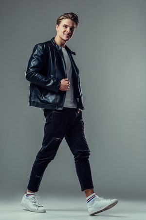 Handsome young man isolated. Fashionable  man in leather jacket is walking on grey background.の写真素材
