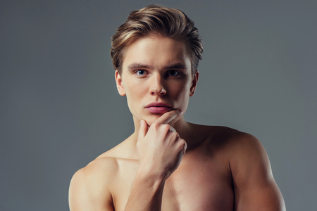 Handsome young man isolated. Portrait of shirtless muscular man is standing on grey background.の写真素材