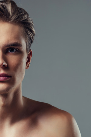 Handsome young man isolated. Cropped image of shirtless muscular man is standing on grey background. Half face.の写真素材