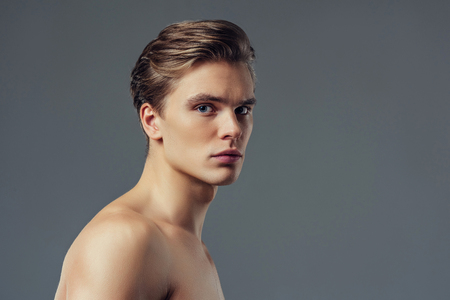 Handsome young man isolated. Portrait of shirtless muscular man is standing on grey background and looking at camera.の写真素材