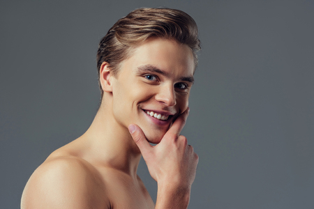 Handsome young man isolated. Portrait of shirtless muscular man is standing on grey background, looking at camera and smiling.の写真素材
