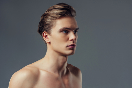 Handsome young man isolated. Portrait of shirtless muscular man is standing on grey background.の写真素材