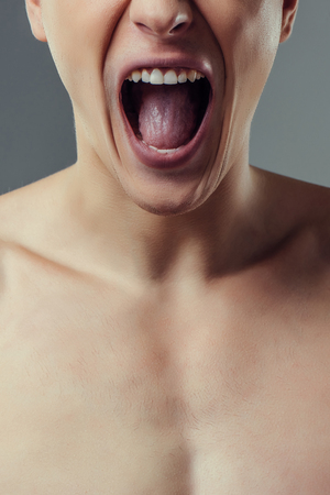 Handsome young man isolated. Cropped image of shirtless muscular man is standing on grey background and shouting. Close-up of men face.の写真素材