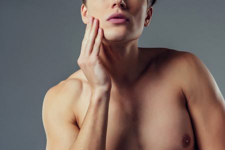 Handsome young man isolated. Cropped image of shirtless muscular man is standing on grey background. Men face care.の写真素材
