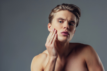 Handsome young man isolated. Portrait of shirtless muscular man is standing on grey background. Men face care.の写真素材