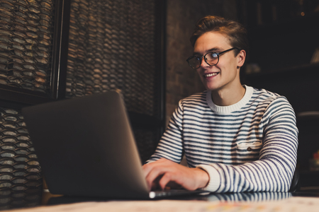 Young handsome man in eyeglasses is working in cafe with laptop.の写真素材