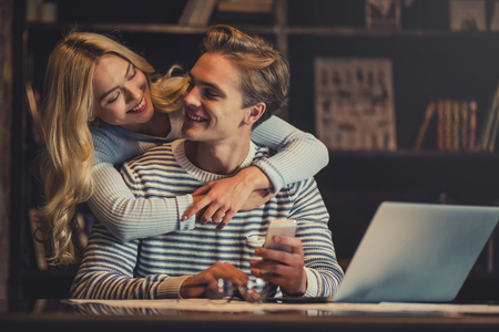 Handsome young man and attractive young woman are hugging while spending time together. Romantic couple is working in cafe.の写真素材