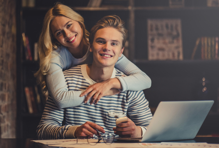 Handsome young man and attractive young woman are hugging while spending time together. Romantic couple is working in cafe.の写真素材