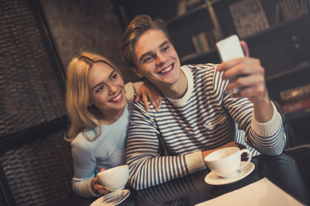 Handsome young man and attractive young woman are spending time together. Couple is working in cafe. Making selfie on smart phone during coffee break.の写真素材