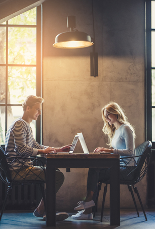Handsome young man and attractive young woman are spending time together. Romantic couple is working in cafe with laptops and mobile phones.の写真素材