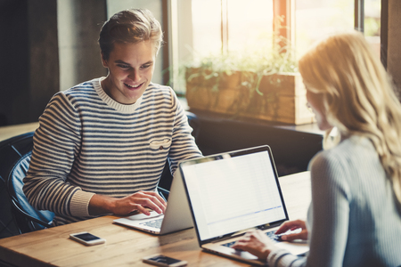 Handsome young man and attractive young woman are spending time together. Romantic couple is working in cafe with laptops and mobile phones.の写真素材