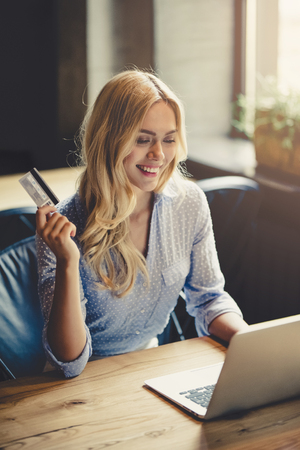 Young attractive businesswoman is working in cafe with laptop. Holding credit card in hand and smiling.の写真素材