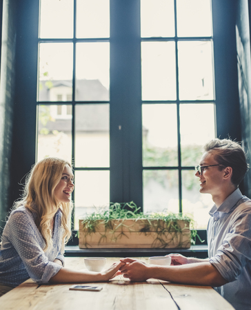 Handsome young man and attractive young woman are spending time together. Romantic couple in cafe is drinking coffee, holding hands and enjoying being together.の写真素材