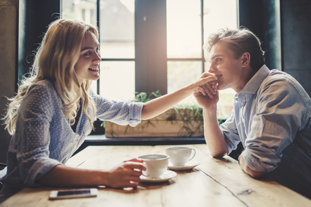 Handsome young man and attractive young woman are spending time together. Romantic couple in cafe is drinking coffee and enjoying being together. Man is kissing hand of his beloved woman.の写真素材