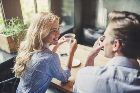 Handsome young man and attractive young woman are spending time together. Romantic couple in cafe is drinking coffee and enjoying being together.の写真素材