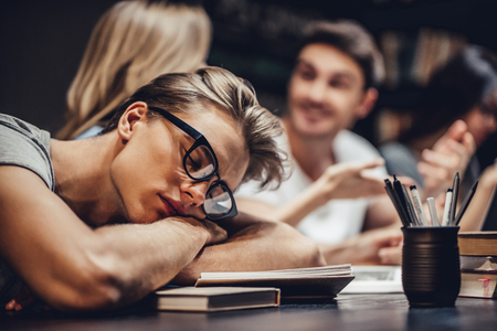 Students are studying in library. Young people are spending time together. Young handsome man fell asleep while working in library.の写真素材